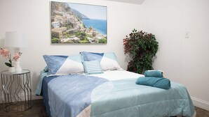 A bedroom with a bed, a nightstand, a lamp, a potted plant, and a painting of a coastal town. - National parks and nice place to relax (Tulare)
