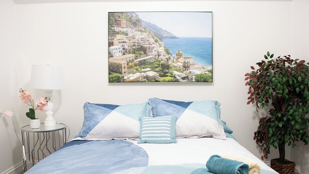 A bedroom with a bed, pillows, a nightstand with a lamp, a framed picture on the wall, and a potted plant. - National parks and nice place to relax (Tulare)