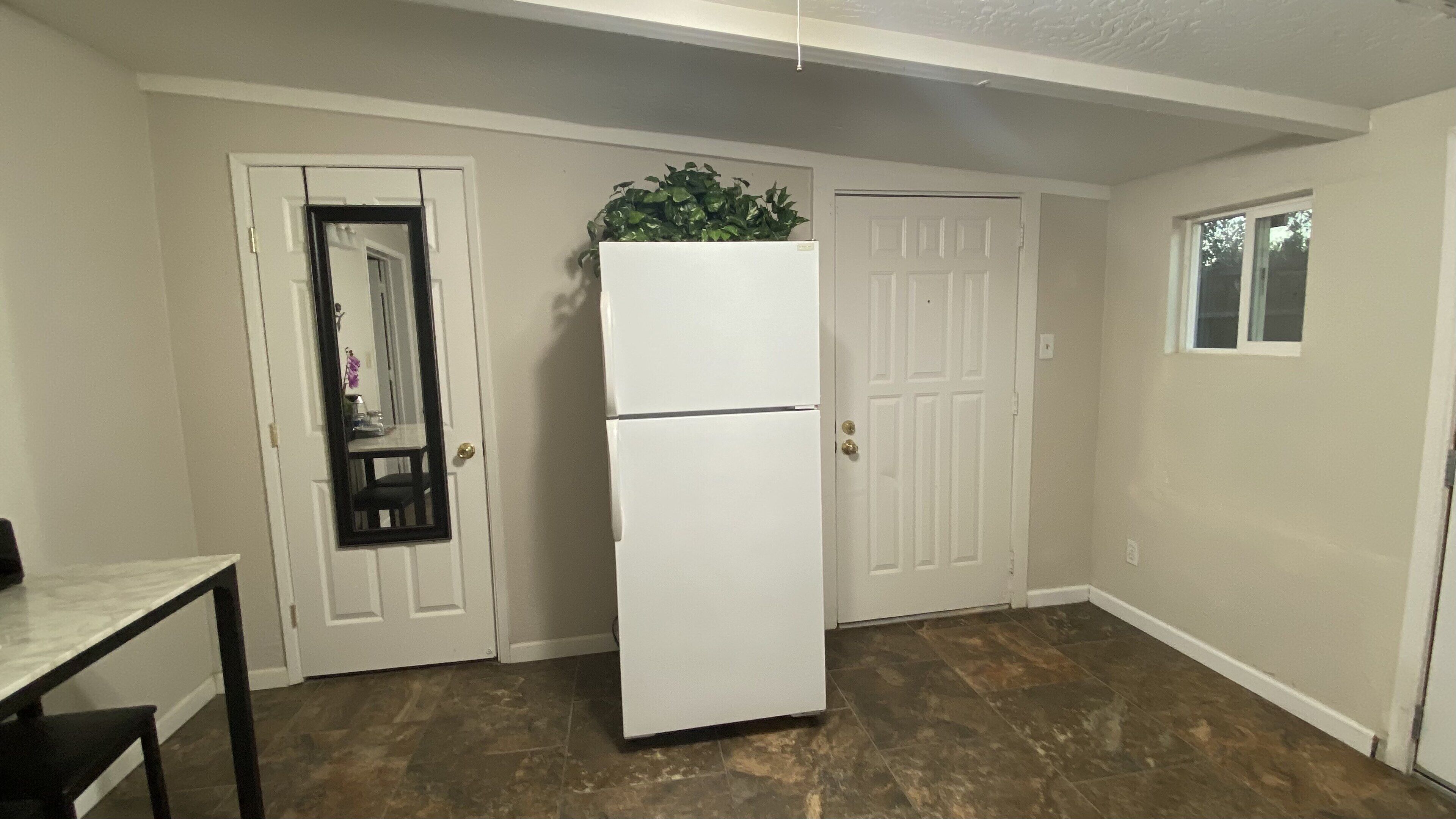 A compact kitchen with a refrigerator, a small table, and a door with a mirror.