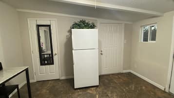 A compact kitchen with a refrigerator, a small table, and a door with a mirror.