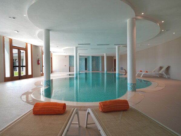 Una amplia piscina cubierta con diseño circular, rodeada de sillones de descanso y vistas despejadas al exterior.