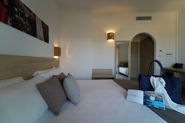 A hotel room with a large bed, a bedside table, a reading lamp, a wall-mounted artwork, and a door leading to another room.
