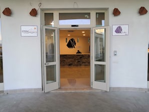 A hotel entrance with glass doors, a reception desk, and a stone wall. - GH Santina Resort (Valledoria)