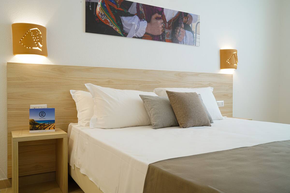 A hotel room with a wooden headboard, white bedding, and two wall-mounted light fixtures.