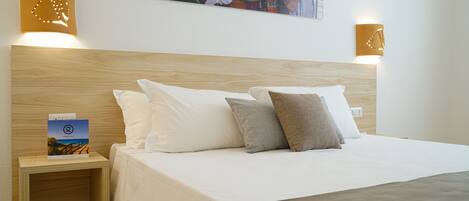 A hotel room with a wooden headboard, white bedding, and two wall-mounted light fixtures.
