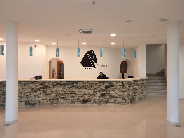 A reception area with a stone wall, a receptionist, and a logo for Santina Resort & Spa.