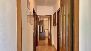 A narrow hallway with tiled flooring, wooden doors, and a kitchen area visible in the distance. - Holiday apartment with sea view and air conditioning (Čižići)