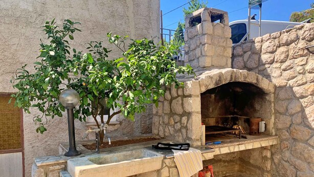 A stone-built outdoor oven with a brick table in front, a metal lamp, and a tree. - Holiday apartment with sea view and air conditioning (Čižići)