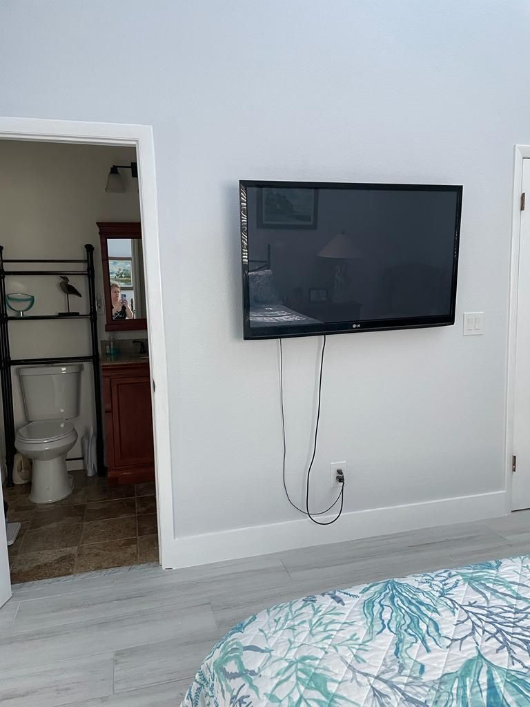 A bedroom with a bed, a television mounted on the wall, a bathroom with a toilet and sink, and a mirror.