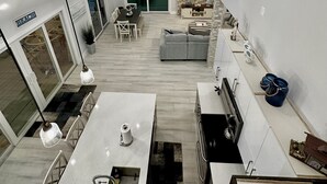 A modern kitchen with a central island, a dining area with a table and chairs, a grey sofa, and a TV mounted on a stone wall. - Breath taking canal, pool home with golf access. 15 minutes from beaches. (Port Charlotte)