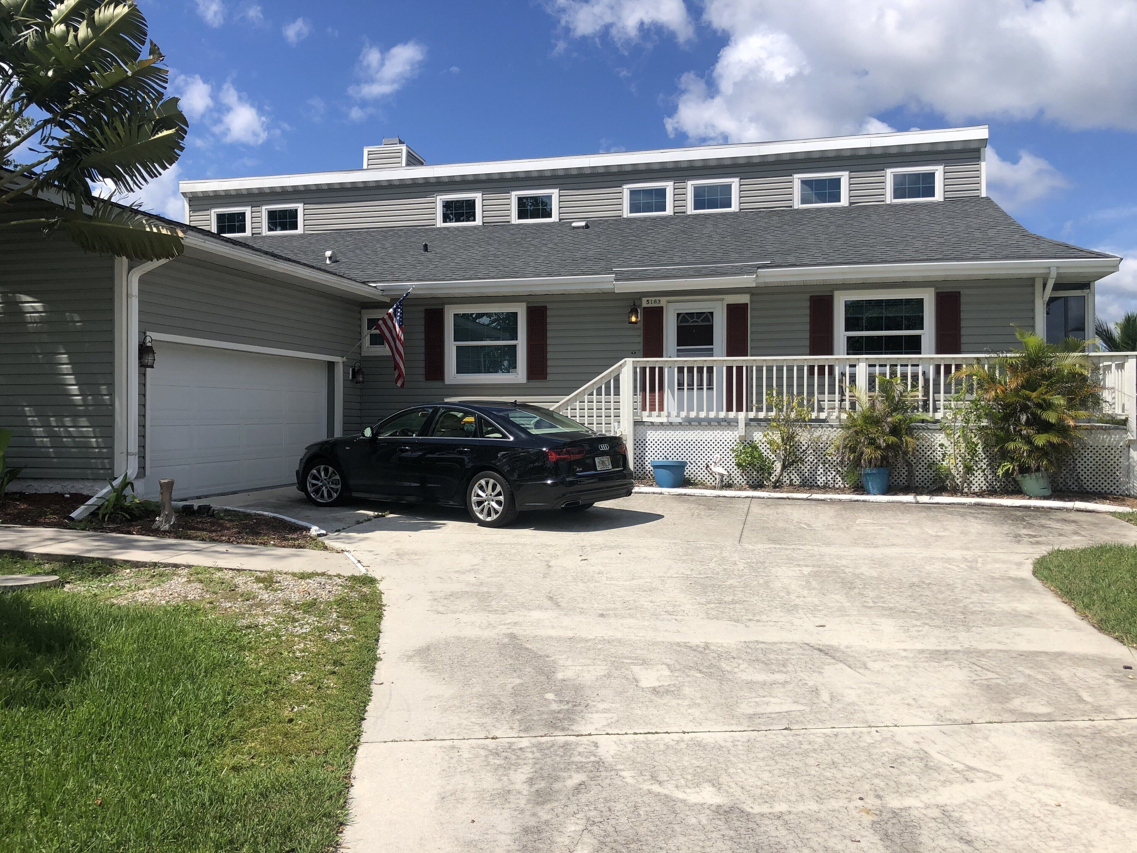 Une maison à deux étages avec un garage, une allée et une véranda à l’avant, dotée d’une balustrade.