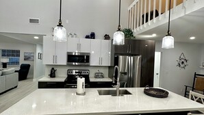 A modern kitchen with white cabinets, stainless steel appliances, and a large island with bar stools. - Breath taking canal, pool home with golf access. 15 minutes from beaches. (Port Charlotte)