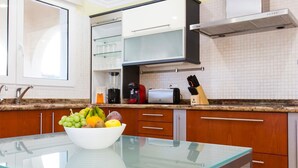 A modern kitchen with a glass table, wooden cabinets, and a built-in oven. - 5 minutes from the beach! Ideal house for families, with private pool. (La Xara)