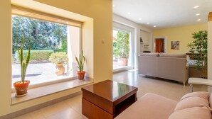 A spacious living room with a sofa, a coffee table, and potted plants near large windows. - 5 minutes from the beach! Ideal house for families, with private pool. (La Xara)