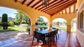 A covered patio with a dining table and chairs, wooden beams, and a view of a swimming pool and greenery. - 5 minutes from the beach! Ideal house for families, with private pool. (La Xara)
