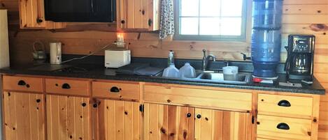 Una cocina de madera con microondas integrado, cafetera y lavamanos.