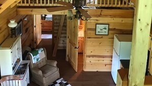 Une chambre mansardée chaleureuse avec un plafond en pente, un ventilateur de plafond, un tapis à carreaux, un canapé et un coin cuisine.