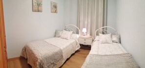 Two single beds with matching headboards and pillows, a nightstand with a lamp, and floral artwork adorn this serene bedroom.