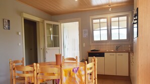 A dining area with a wooden table and chairs, a kitchen with cabinets and a window, and a door leading to another room. - Villa near Les Vans Centre (Les Vans)