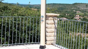 A balcony with a stone pillar and metal railing overlooking a hilly landscape with greenery and buildings. - Villa near Les Vans Centre (Les Vans)