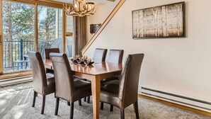 A dining area with a wooden table and leather chairs, large windows, and a chandelier. - Newly Updated Condo, Pool & Hot Tub, Shuttle to Slopes, Large Private Patio (Keystone)
