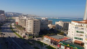 A coastal cityscape with modern buildings, a clear blue sky, and a view of the sea.