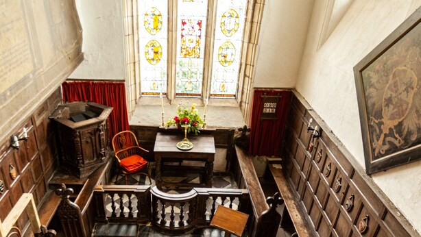 Ein Kircheninneres mit Schachbrettfußboden, Holzbänken, einem Glasfenster und einem hölzernen Altar.
