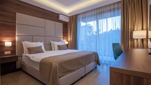 Habitación de hotel con una cama grande, un escritorio, una silla y un ventanal con cortinas.