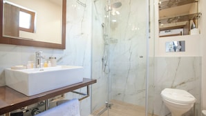 Un baño moderno con un lavamanos grande y blanco, una ducha con cerramiento de vidrio y un inodoro.