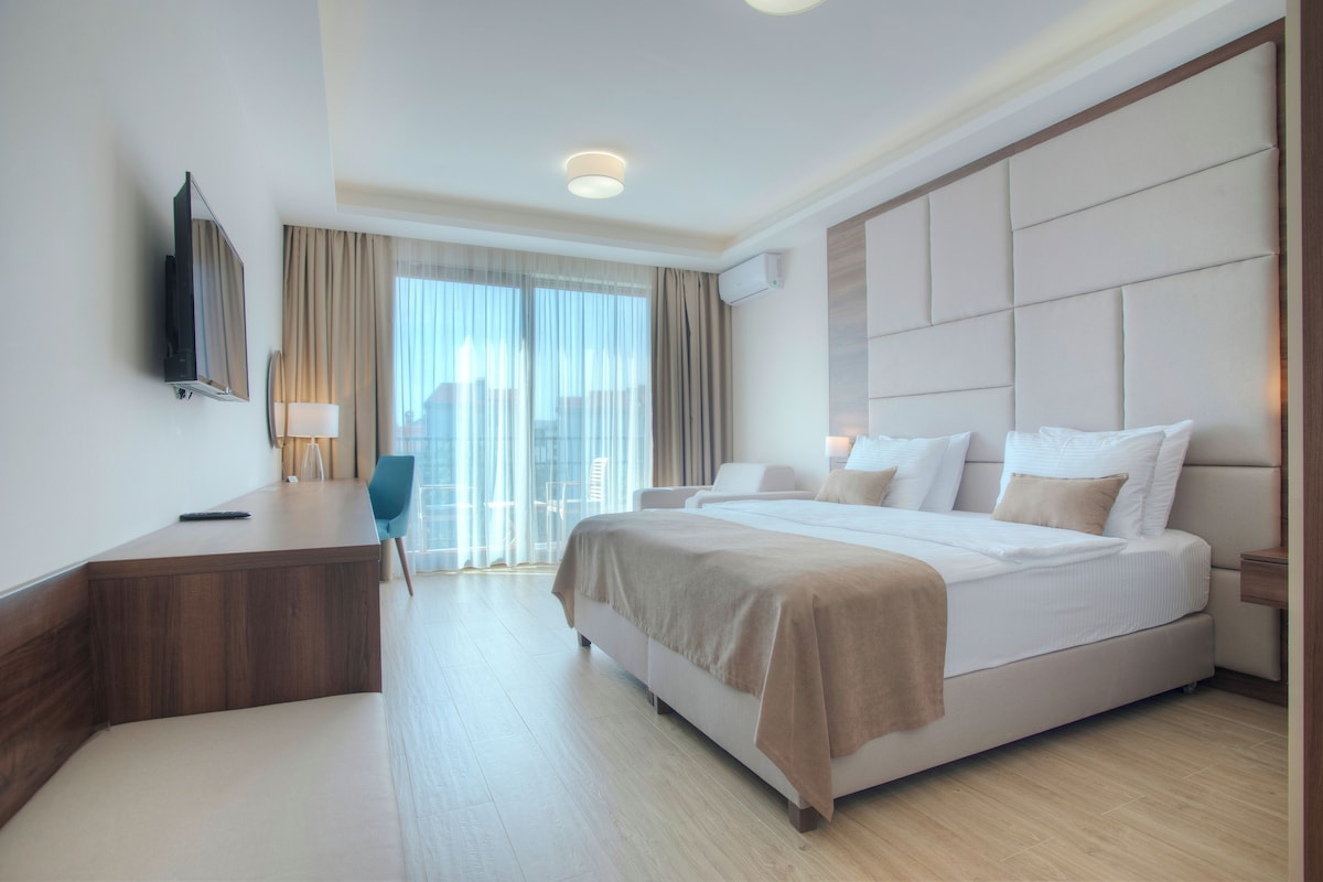 Una habitación de hotel moderna con una cama grande, un escritorio, una silla, un televisor y una ventana con cortinas.