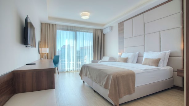 Una habitación de hotel moderna con una cama grande, un escritorio, una silla, un televisor y una ventana con cortinas.