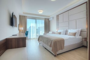 A modern hotel room with a large bed, a desk, a chair, a TV, and a window with curtains.