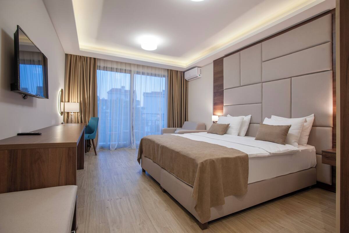 A modern hotel room with a large bed, a desk, a chair, and a television.