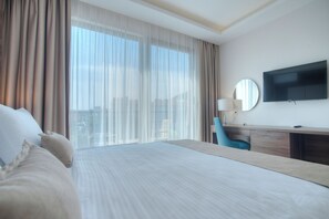 A hotel room with a large bed, a desk, a chair, a TV, and a window with curtains.