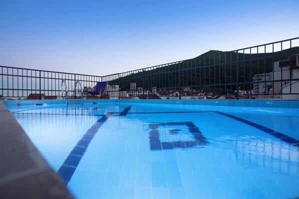 A swimming pool with clear water, a blue sky, and a mountainous backdrop.
