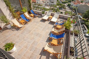 A rooftop terrace with multiple lounge chairs and tables, surrounded by potted plants and a view of the cityscape. - Twelve (Budva)