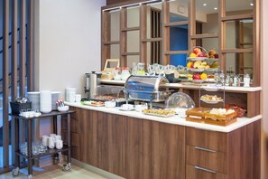 A buffet setup with various food items, a beverage station, and a glassware cart.