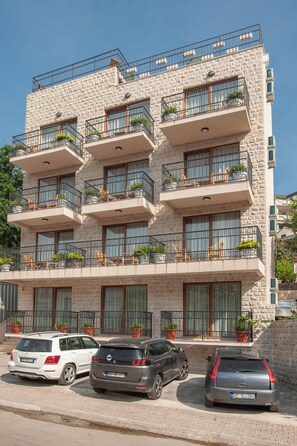 A multi-story building with balconies, potted plants, and parked cars.