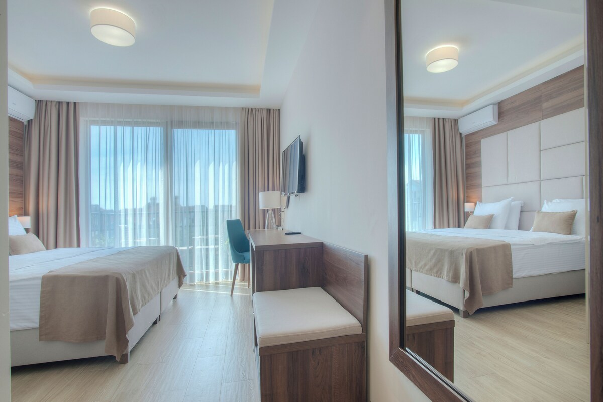 A hotel room with two beds, a desk, a chair, a TV, and a large mirror.
