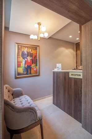 A reception desk with a 'RECEPTION' sign, a framed family photo on the wall, a tufted chair, and a modern light fixture.