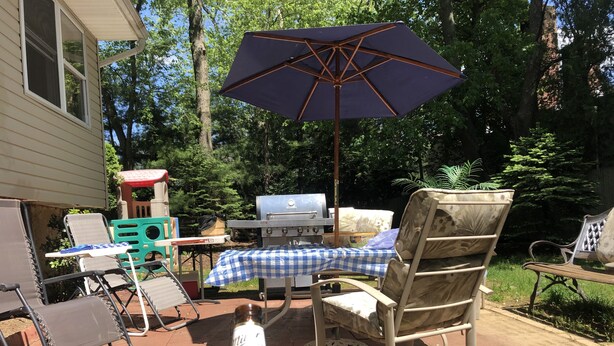 An outdoor patio with a grill, folding chairs, and a table with a checkered tablecloth.