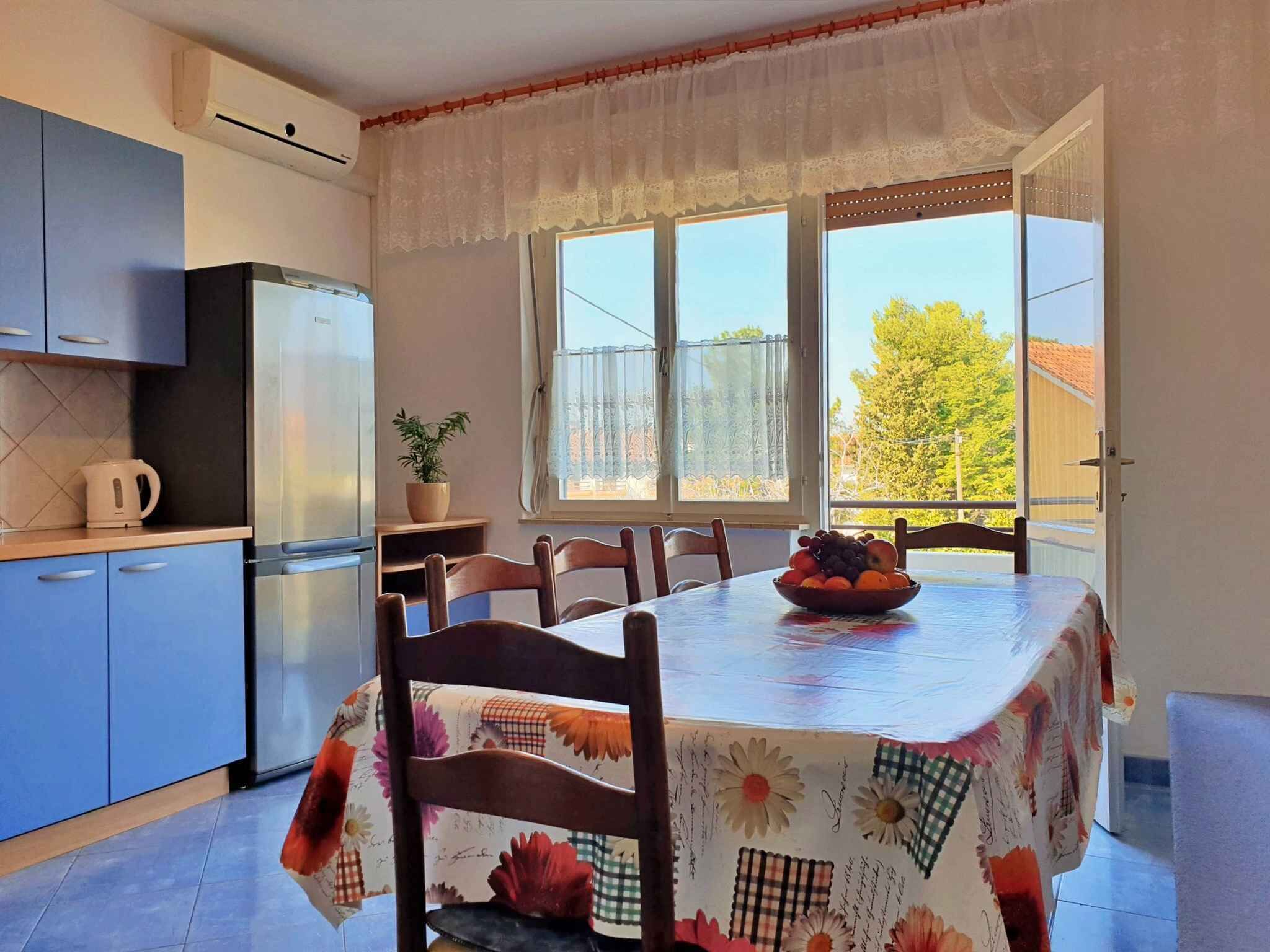 A kitchen with a dining table, chairs, a refrigerator, and a potted plant.