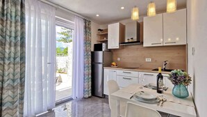 A modern kitchen with white cabinets, a stainless steel refrigerator, and a dining area with a table set for two. - Holiday flat with sea view just 60 m from the beach (Šilo)