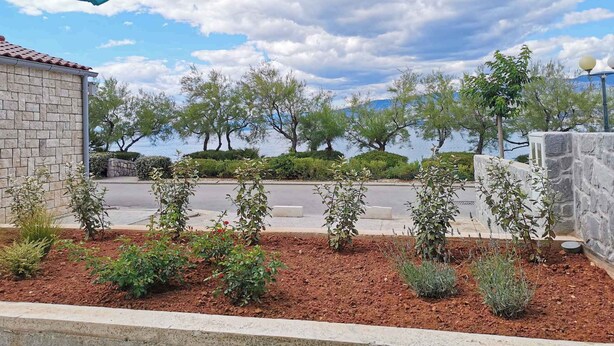 A landscaped garden with a stone wall, a paved area, and a view of a body of water. - Holiday flat with sea view just 60 m from the beach (Šilo)