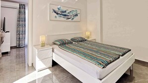 A modern bedroom with a white bed, striped bedding, two bedside lamps, and a ceiling light. - Holiday flat with sea view just 60 m from the beach (Šilo)