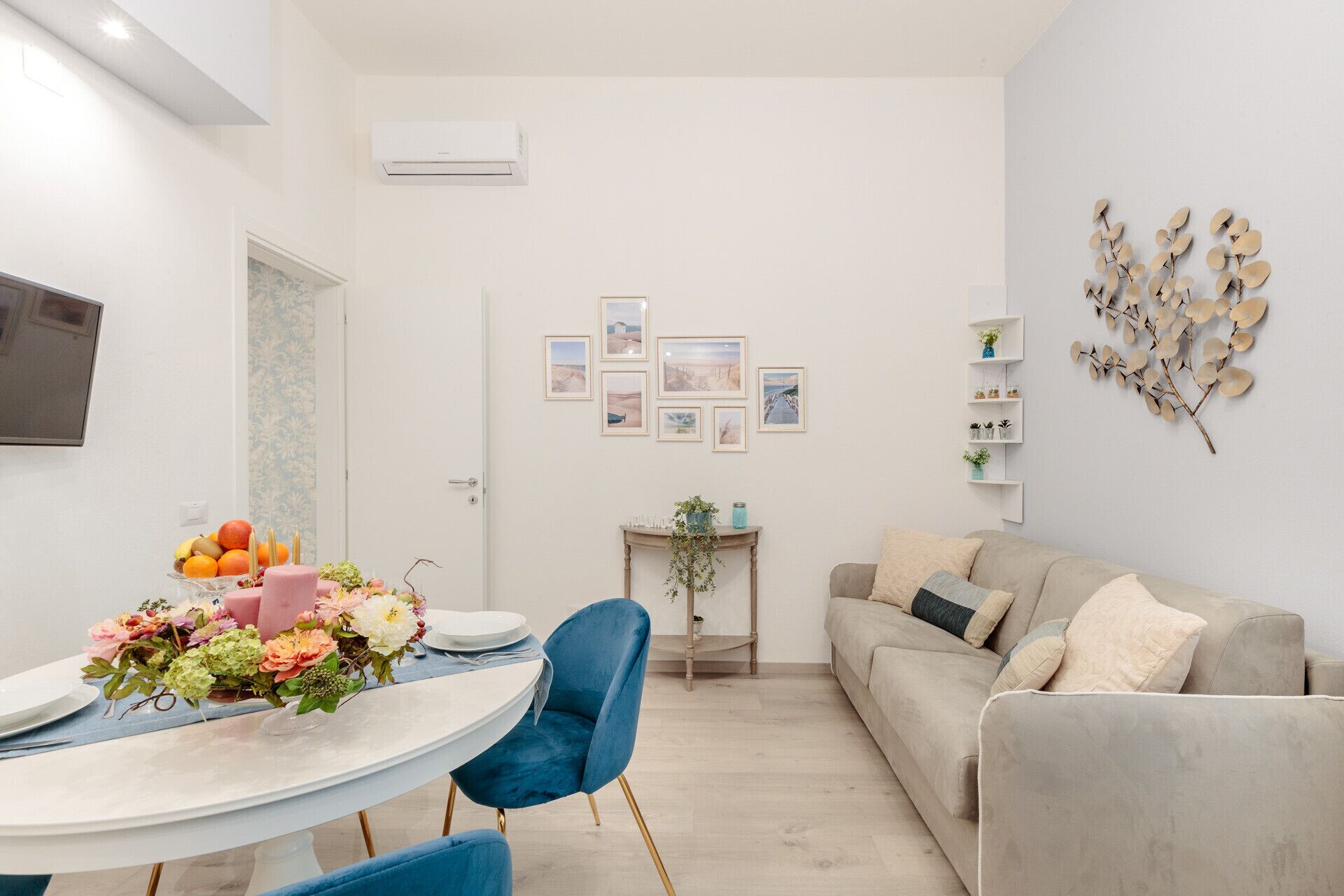 A modern living room with a beige sofa, a round dining table with chairs, and a small side table with a vase.