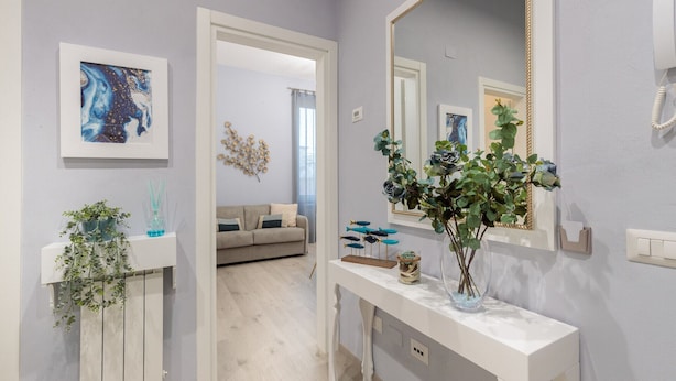 A hallway with a white console table, a mirror, and a plant. There is a sofa in the background.