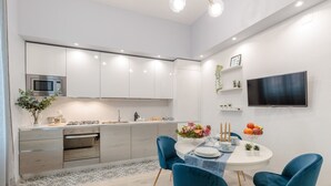 A modern kitchen with white cabinets, a built-in microwave, and a dining area with blue chairs and a white table.