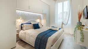 A modern bedroom with a large bed, white walls, and a window with sheer curtains.