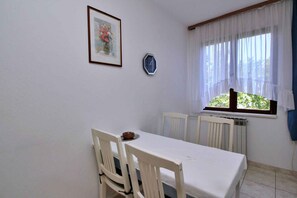Simple, functional room with a single table, chair, and framed picture, offering a view of greenery outside.